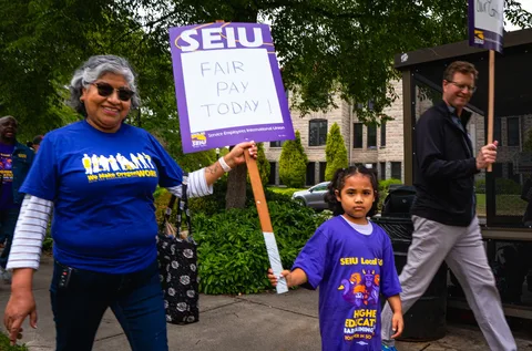 A Local 083 member and a child carry an SEIU sign reading Fair Pay Today during the June 30 rally