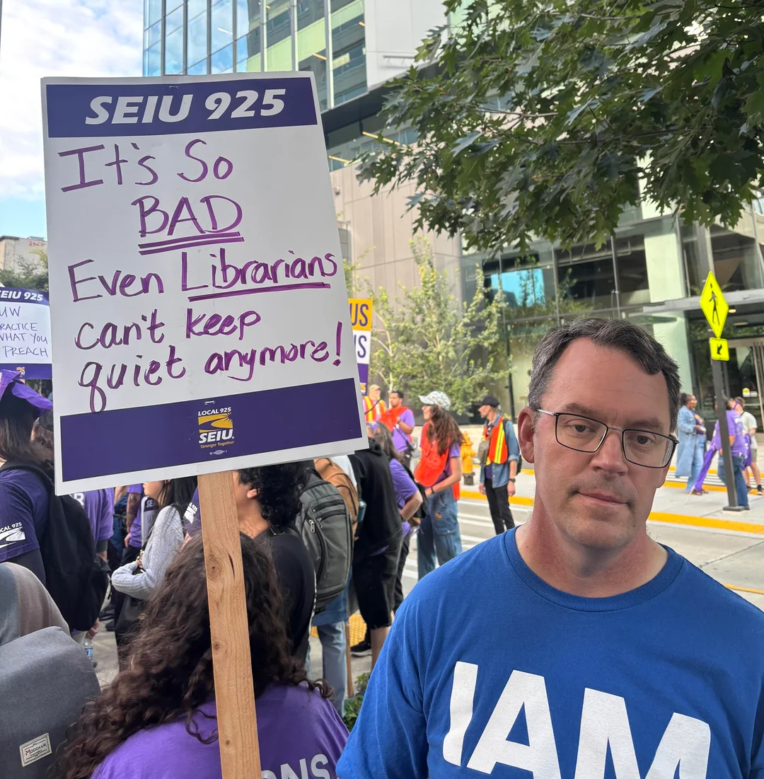 Marcher beside an SEIU 925 sign reading “It’s so bad even librarians can’t keep quiet anymore!”